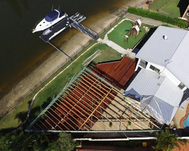 Aerial view of a canal-front home with a large deck being framed beside a private boat berth