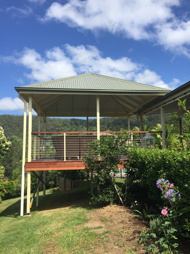Elevated hardwood deck with a wire balustrade and gabled roof over a hinterland garden