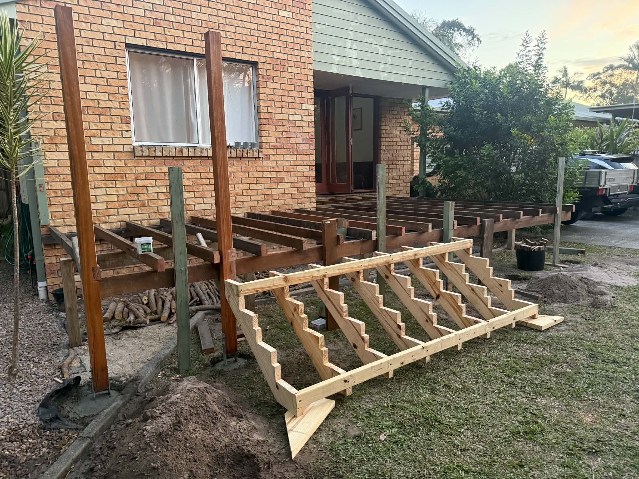 Hardwood deck substructure framed against a brick home, with a freshly built timber stair stringer set in the foreground