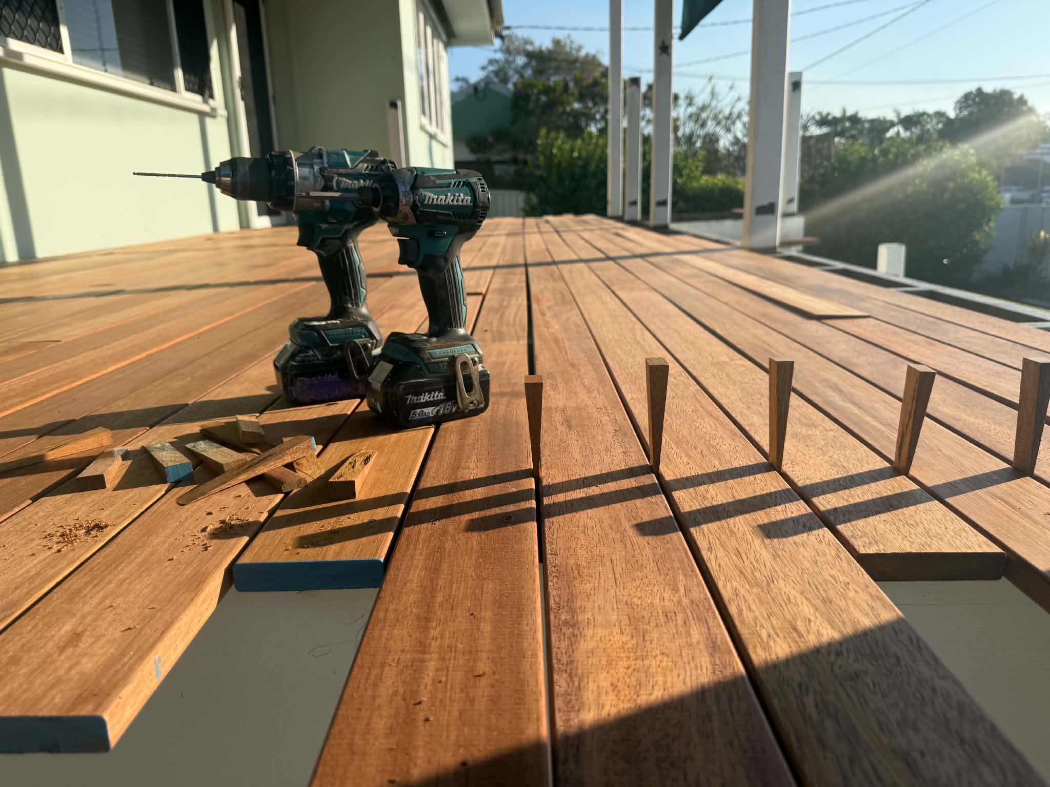 Freshly laid hardwood deck boards catching golden afternoon light, with cordless drills and timber plugs sitting on the deck
